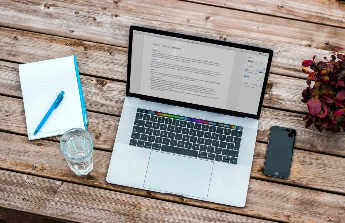 Önéletrajz szerkesztése laptopon, mellette jegyzetfüzet, toll és telefon egy fa asztalon